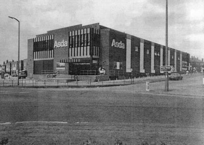 Black and white image of a two story brick building with ASDA logo on side and front